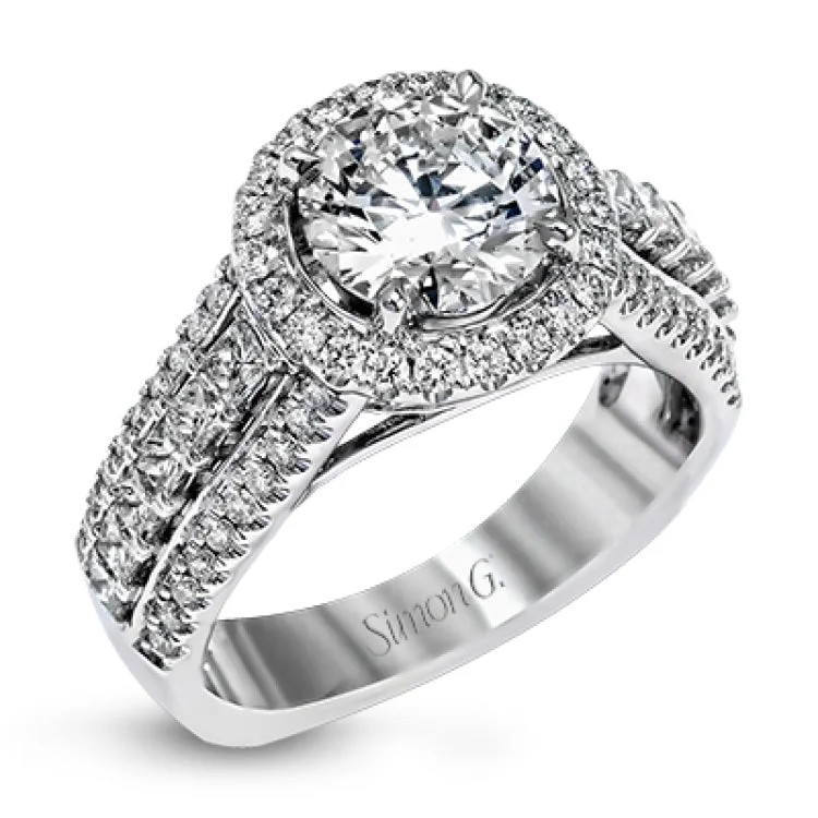 This bold engagement ring in 18K has a round halo, a cathedral design, and showcases PC diamonds 0.53 ctw. outlined by 2 rows of RD diamonds 0.46 ctw. on the shank, & accented with pave diamonds on the profile.