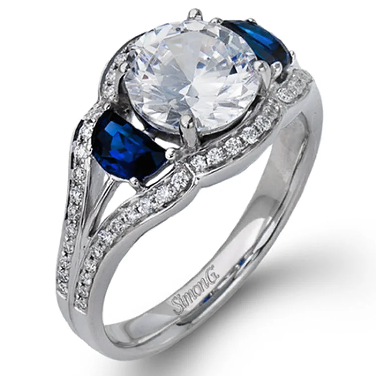 This unique 18K engagement ring features a 3-stone design & takes a RD center with 2 moon cut sapphires 0.79 ctw, and is outlined by round white diamonds 0.23 ctw.